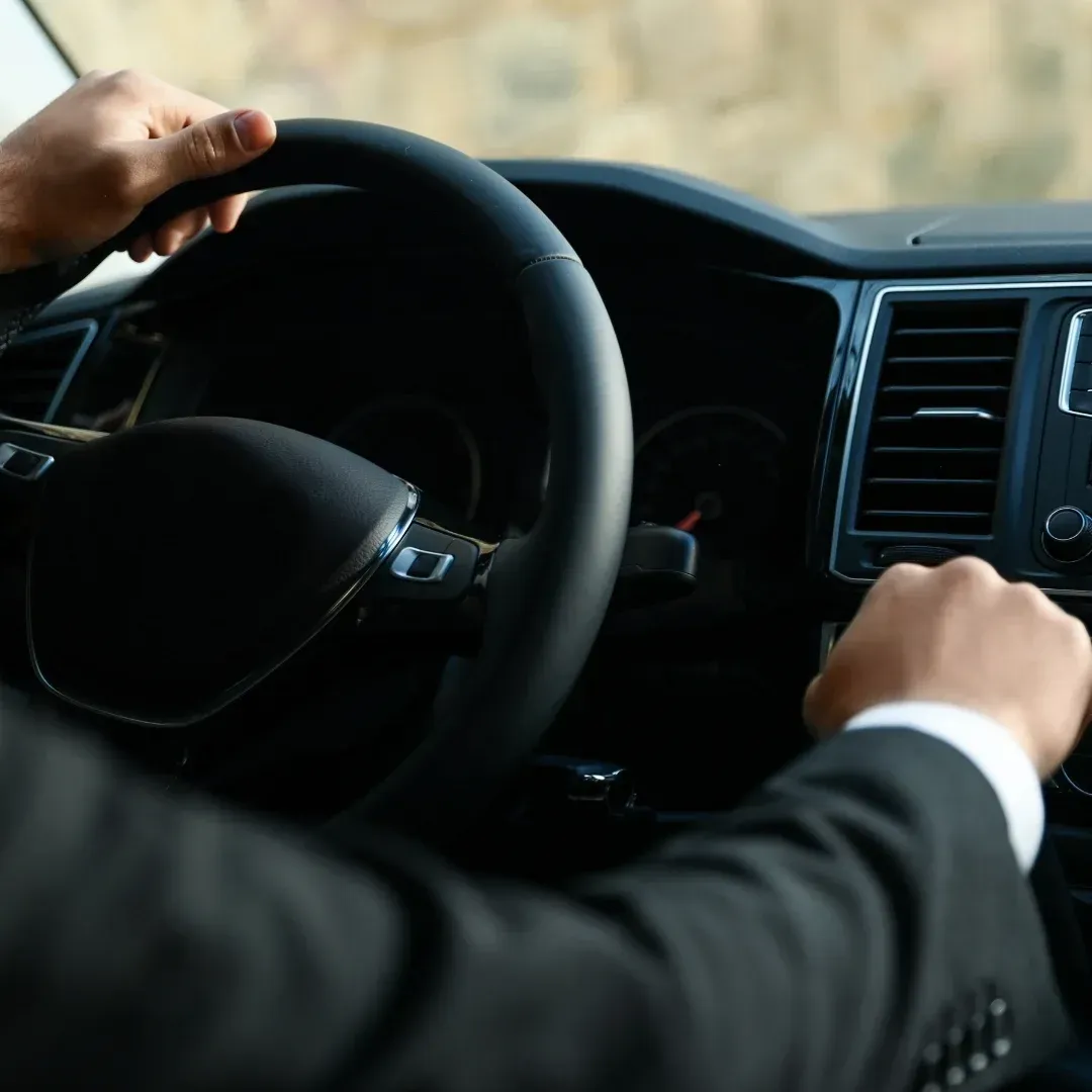Driver’s hands on a car steering wheel and dashboard, viewed from inside the vehicle.