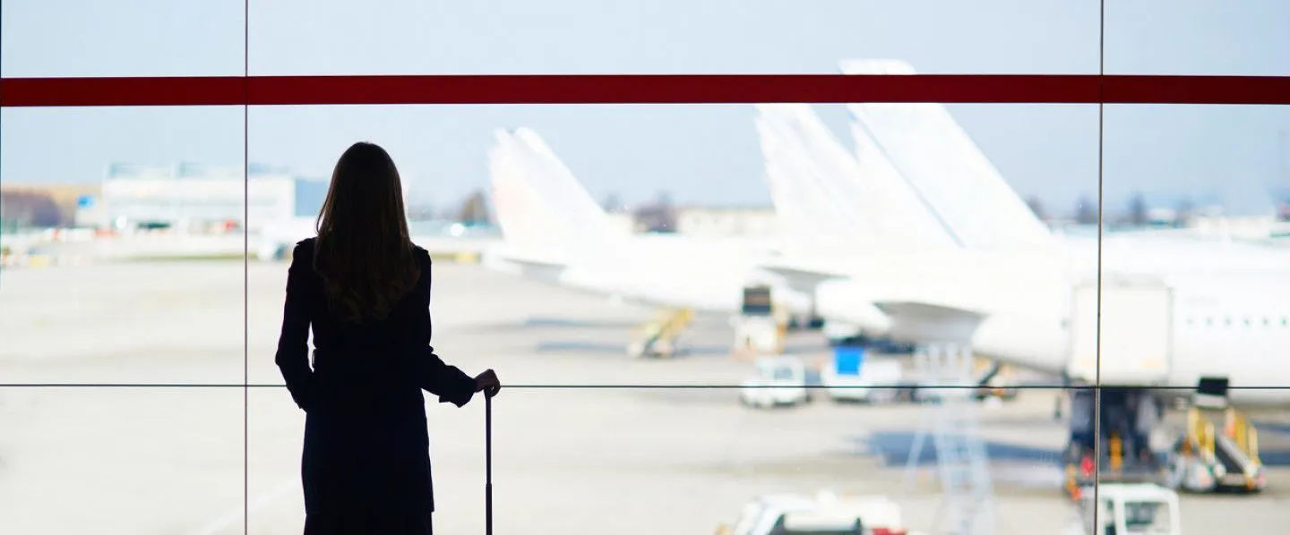 A woman is standing in front of a window at an airport looking out at planes.