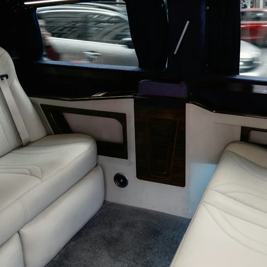 Luxury car interior with white leather seats, gray carpet, and dark wood trim by the window