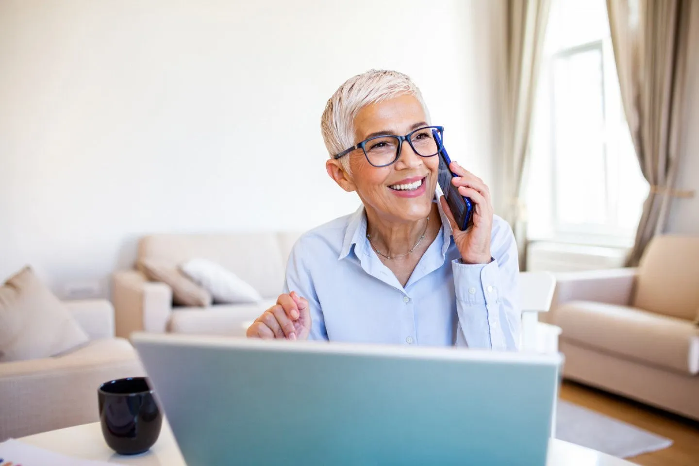 A woman is sitting in front of a laptop computer talking on a cell phone.