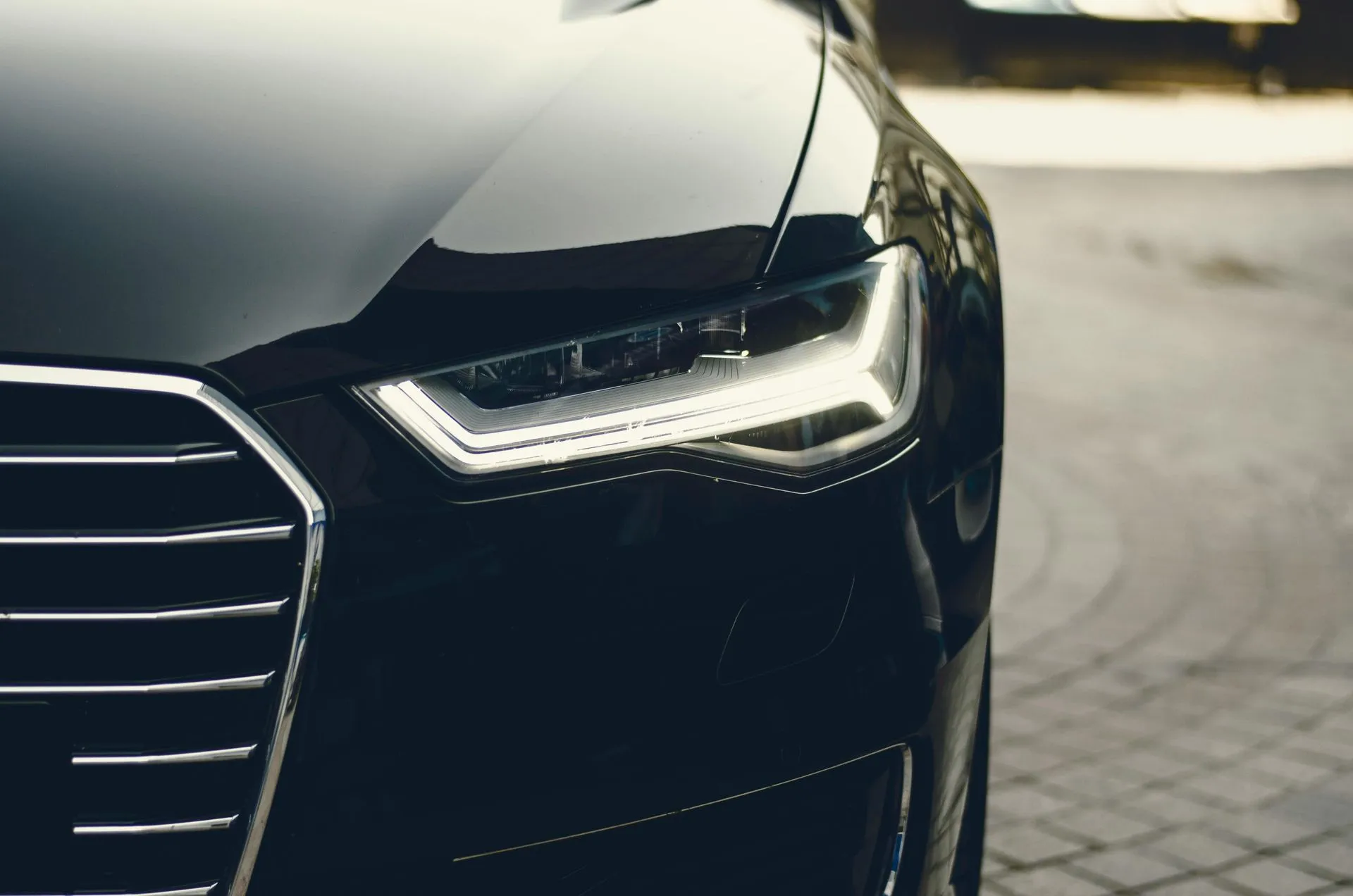A close up of a black car parked on a cobblestone street.